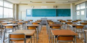 An empty classroom with wood desks and a chalk board at the front. 